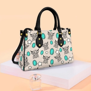 Close-up of cream PU crossbody bag with highland cow print and black handles
