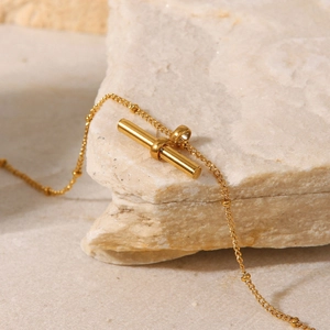 Macro view of 18K gold titanium steel anklet with T-bar pendant on natural stone base