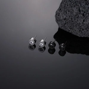Macro shot of silver and black titanium steel stud earrings with cubic zirconia on black mirror
