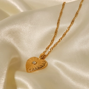 Macro shot of gold heart pendant with zircon on a white satin fabric background
