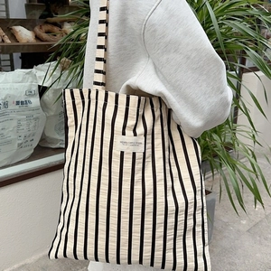 Classic black and white striped canvas tote bag with long shoulder strap worn by a model