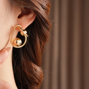 Close-up of a twisted gold metallic earring with spherical accents on a female model