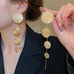 Close-up of long gold fringe earrings with textured metal discs on model