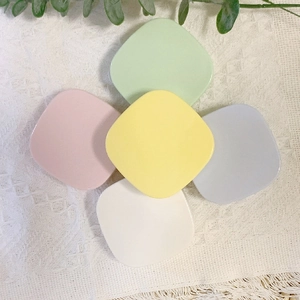 Flat lay of macaron-colored square contact lens cases on a white woven tablecloth