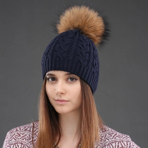 Detail of navy blue cable knit wool hat featuring a fluffy brown faux fur pom-pom topper