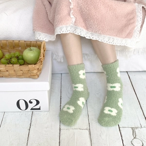 Close-up of green plush socks with white floral patterns worn in a cozy indoor setting