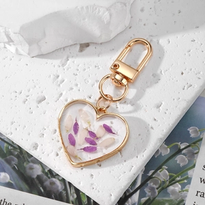 Golden heart keychain with real dried flowers and resin pendant on a textured stone