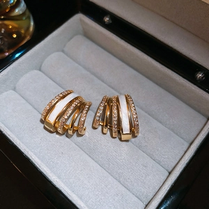Close-up detail of gold-plated C-shaped earrings with white enamel and sparkling zircon stones