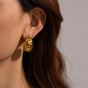 Macro detail of gold-plated drop earrings featuring a unique hammered lava texture