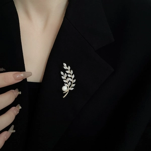 Detail of wheat ear brooch with gold plating, sparkling zircons and large pearl on a suit