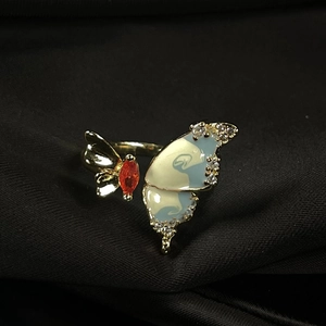 Macro view of gold butterfly ring with white enamel and orange marquise gemstone detail