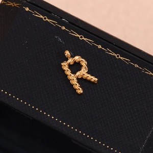 Macro shot of twisted rope texture letter R pendant in 18K gold on black jewelry box