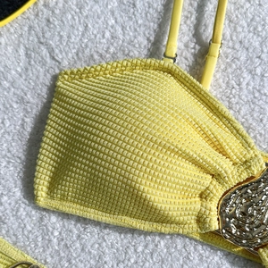 Macro detail of yellow seersucker bikini fabric with adjustable strap and gold metal buckle