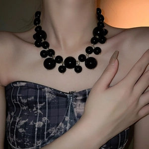 Close-up of oversized glossy black faux pearl choker with gold connectors on neck