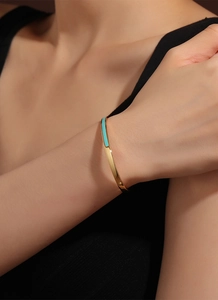 Detail of minimalist gold-plated bangle featuring polished finish and sky blue enamel inlay