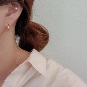 Close-up of a model wearing a minimalist gold hoop earring and round white pearl stud set