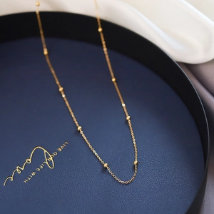 Collier à billes dorées minimaliste sur un plateau bleu marine avec un fond en tissu blanc