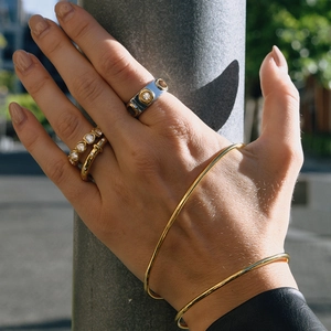 Close-up of gold layered rings and slim bangle bracelet under natural sunlight