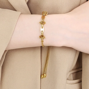 Detail of gold knot chain bracelet with tassel charms worn over a khaki blazer sleeve