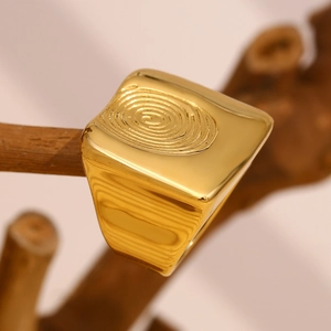 Detail eines 18K vergoldeten quadratischen Rings mit Fingerabdruck-Muster auf einem Ast