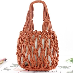 Handmade orange woven cotton rope handbag with beige inner lining on a tropical leaf background