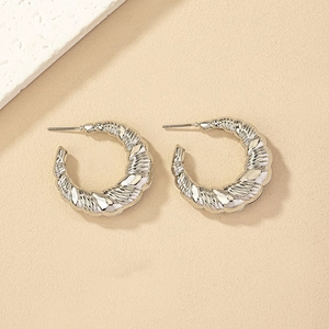Detailed macro view of silver twisted croissant hoop earrings on a beige textured background