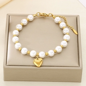 Detail of gold beaded bracelet with white pearls and a heart pendant on a display box