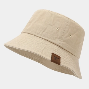 Dettaglio di un cappello pescatore in tela beige con etichetta in pelle e cuciture fini