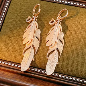 Elegant rose gold feather drop earrings with sparkling rhinestones on a velvet background