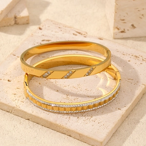 Two gold stainless steel bangles with zircon stone inlay on a textured stone base