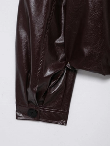 Macro detail of dark burgundy faux leather jacket cuff with a single black button