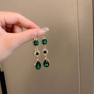 Detail of vintage emerald green long earrings with gold teardrop drop in hand