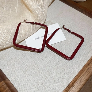 Close-up of geometric diamond-shaped drop earrings with deep red enamel finish