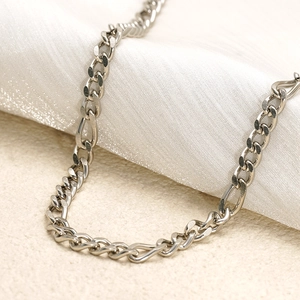 Detailed view of silver stainless steel Figaro chain on soft white satin background