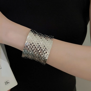 Detail of a wide silver braided metal cuff bracelet featuring a textured geometric pattern