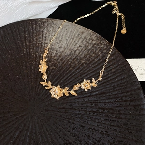 Close-up of golden floral necklace with white zircon inlays on dark ceramic plate