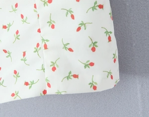 Close-up of floral print fabric with red rosebuds and green leaves on white base