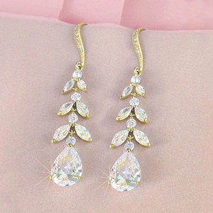 Elegant gold leaf dangle earrings with pear-shaped cubic zirconia on pink fabric