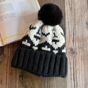 Detail of knit beanie with geometric jacquard pattern and a large black faux fur pom-pom