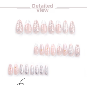 Detailed view of pink almond press-on nails with silver heart patterns and 3D rhinestones
