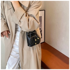 Detail of a mini black quilted bucket bag with gold hardware worn on a beige trench coat