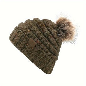 Détail de la maille épaisse d'un bonnet olive avec pompon en fausse fourrure