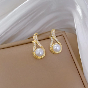 Close-up of golden pearl earrings with shimmering pavé zircon on silk background