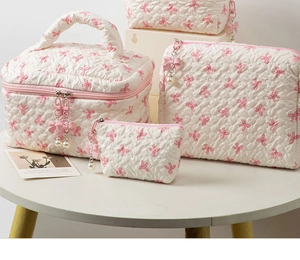 Detailed set of three white quilted makeup bags with pink bow pattern and pearl zipper