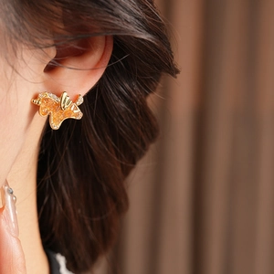Close-up of golden butterfly earring with amber stones and rhinestones on ear
