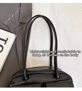 Close-up of black glossy leather shoulder bag with sleek handles on a grey blazer background