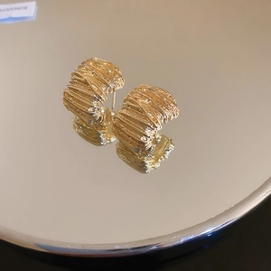 Macro shot of gold wide earrings with irregular pleated texture on a mirror surface