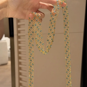 Macro detail of a long golden mesh necklace featuring light blue transparent beads