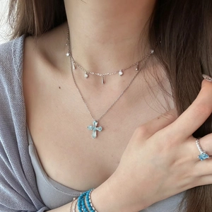 Detail of layered silver necklaces with a light blue cross pendant and matching jewelry set