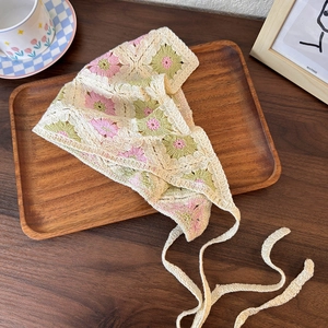 Close-up of handmade crochet bandana featuring beige floral knit patterns and woven ties